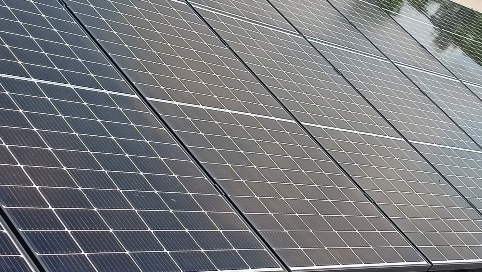 Rząd paneli fotowoltaicznych, widok z dołu pod kątem, ukazujący strukturę krzemową i odbicia nieba na powierzchni.