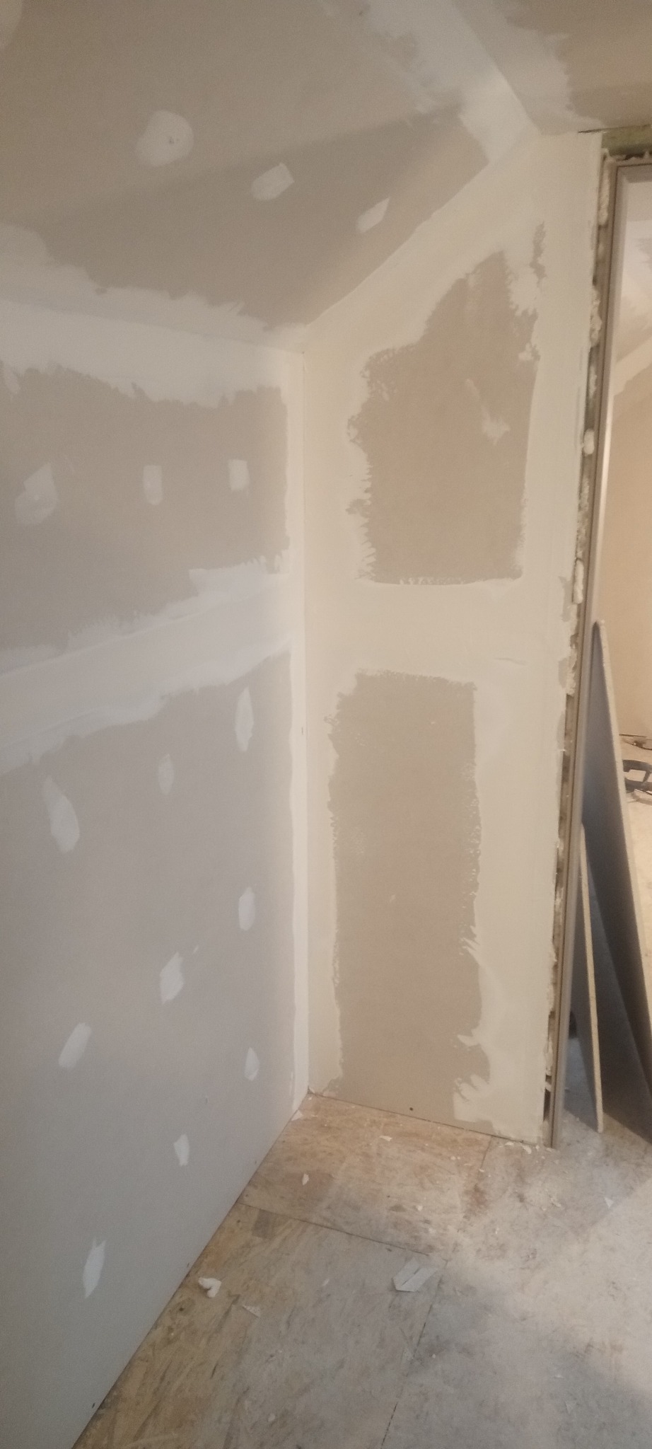 Wnętrze w trakcie prac wykończeniowych: ściany z płyt kartonowo-gipsowych, częściowo wyszpachlowane, widoczne łączenia i nierówności, surowa podłoga z płyt OSB.