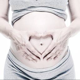 Karolina Bukowska - Ciążowy brzuszek w szarym dresie, dłonie ułożone w kształt serca, delikatna obróbka w chłodnej tonacji.