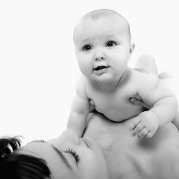 Karolina Bukowska - Czarno-białe ujęcie matki leżącej na plecach z noworodkiem na piersi, skupiające się na delikatnym kontakcie i wyrazie twarzy dziecka.