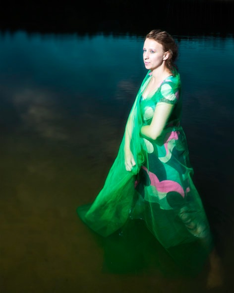 Kobieta w zielonej, wzorzystej sukience i narzutce stoi w wodzie jeziora, zamyślona poza i naturalne światło.