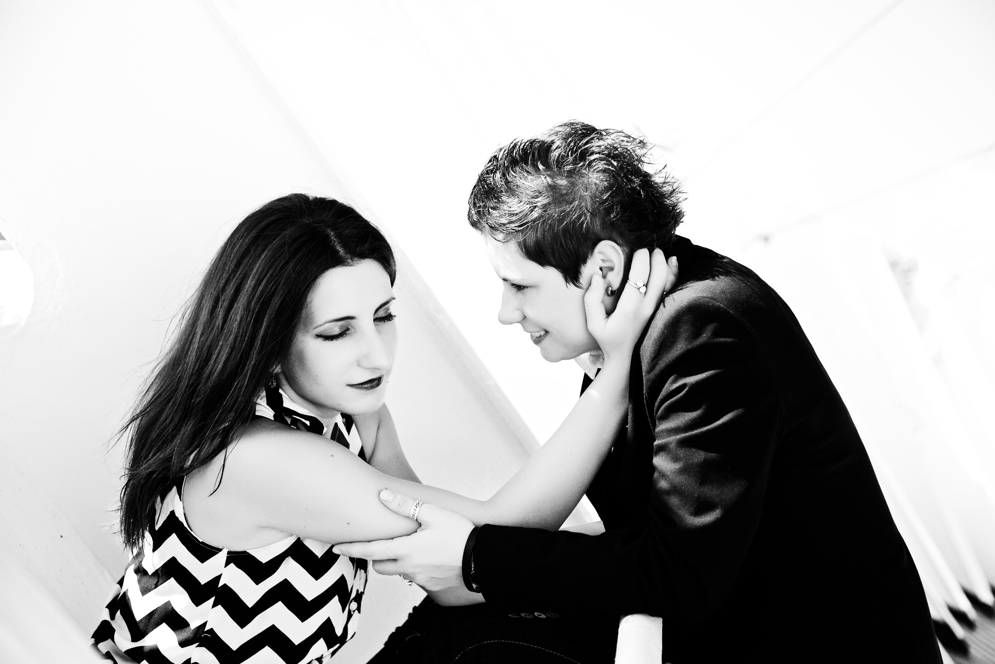 Czarno-białe zdjęcie pary w plenerze: kobieta w bluzce w zygzaki patrzy w dół, mężczyzna w marynarce spogląda na nią z uśmiechem, delikatnie dotykając jej ramienia.