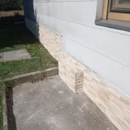 Wykończenie elewacji budynku płytkami imitującymi piaskowiec, widoczne połączenie z szarą ścianą i betonowym chodnikiem.