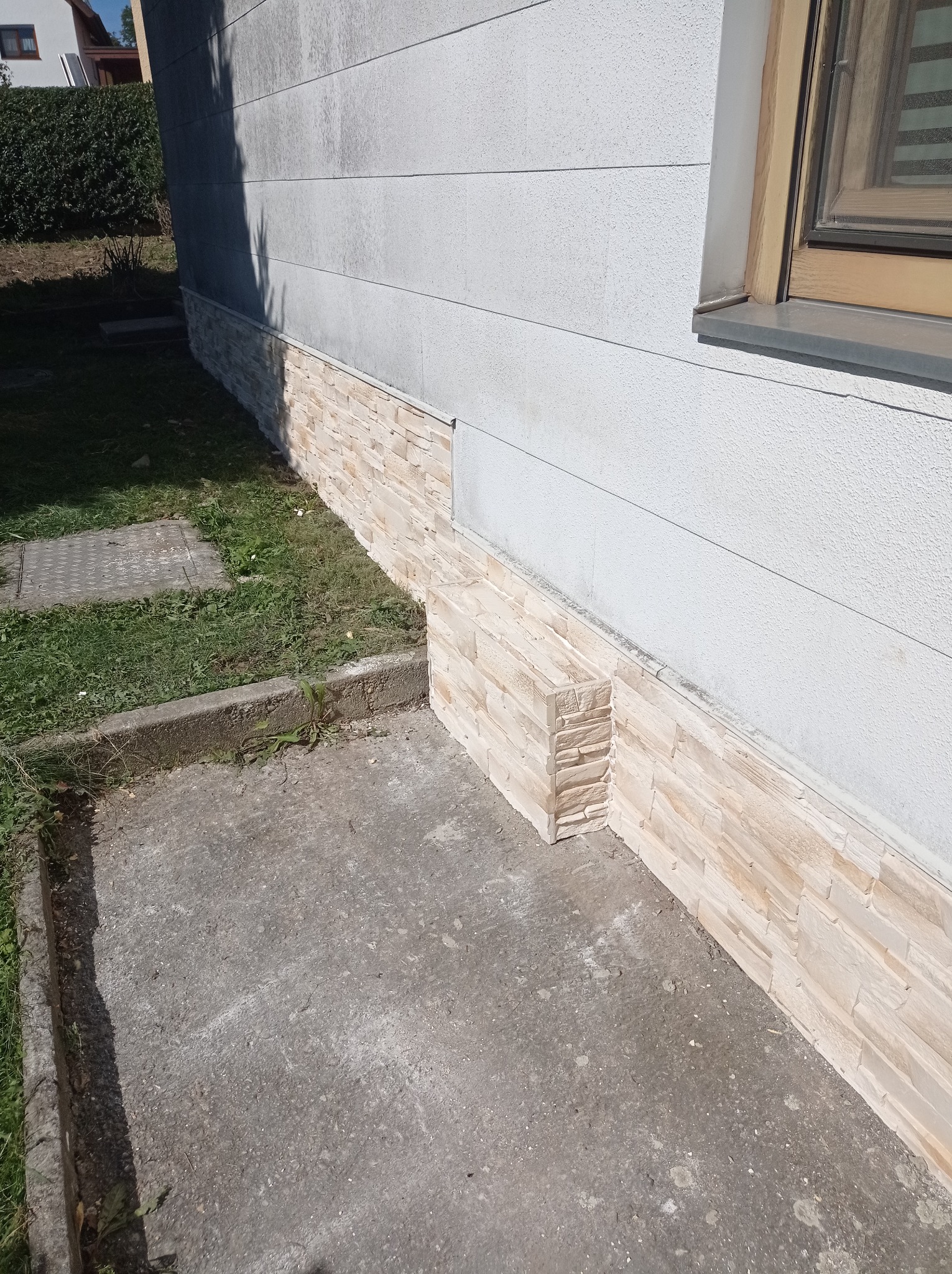 Wykończenie elewacji budynku płytkami imitującymi piaskowiec, widoczne połączenie z szarą ścianą i betonowym chodnikiem.