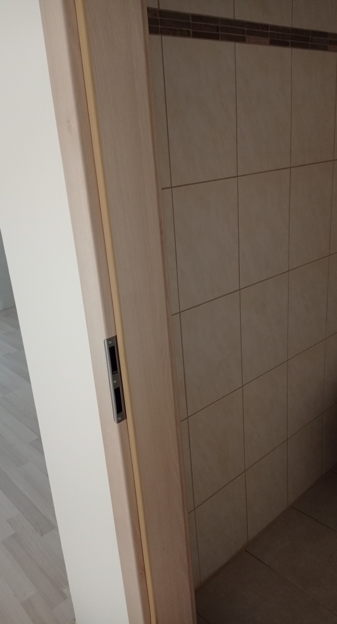 Zamknięte drzwi wewnętrzne z zamkiem wpuszczanym, widoczne płytki ceramiczne na ścianie i podłodze, Toruń.