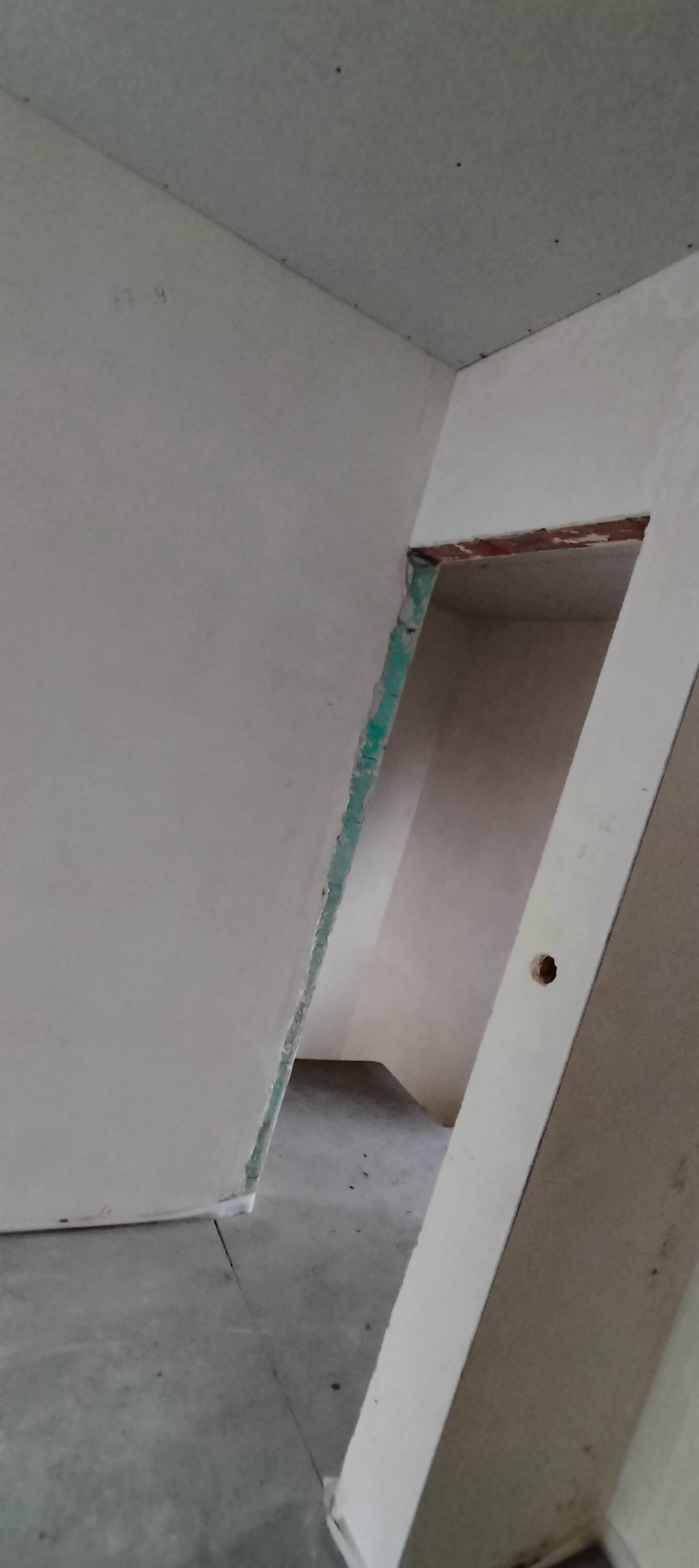 Surowe wnętrze w trakcie prac wykończeniowych: ściany i sufit pokryte płytami gipsowo-kartonowymi, widoczne niedoskonałości i szczeliny, przygotowanie do dalszych etapów prac.