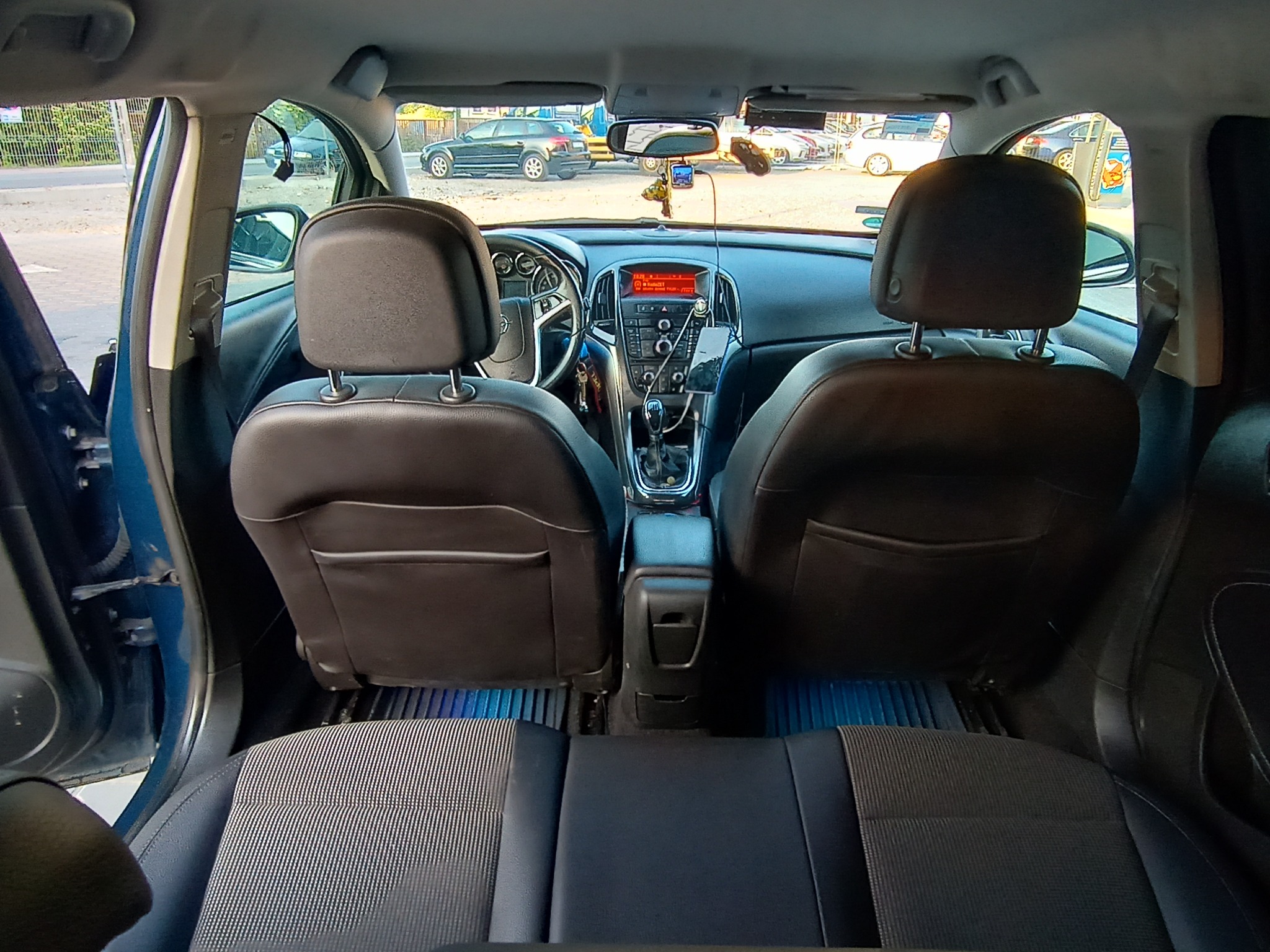 Wnętrze samochodu Opel Astra z widocznymi czarnymi skórzanymi fotelami, deską rozdzielczą z wyświetlaczem radia, kierownicą oraz elementami wyposażenia wnętrza; widok z tylnej kanapy na przód pojazdu.