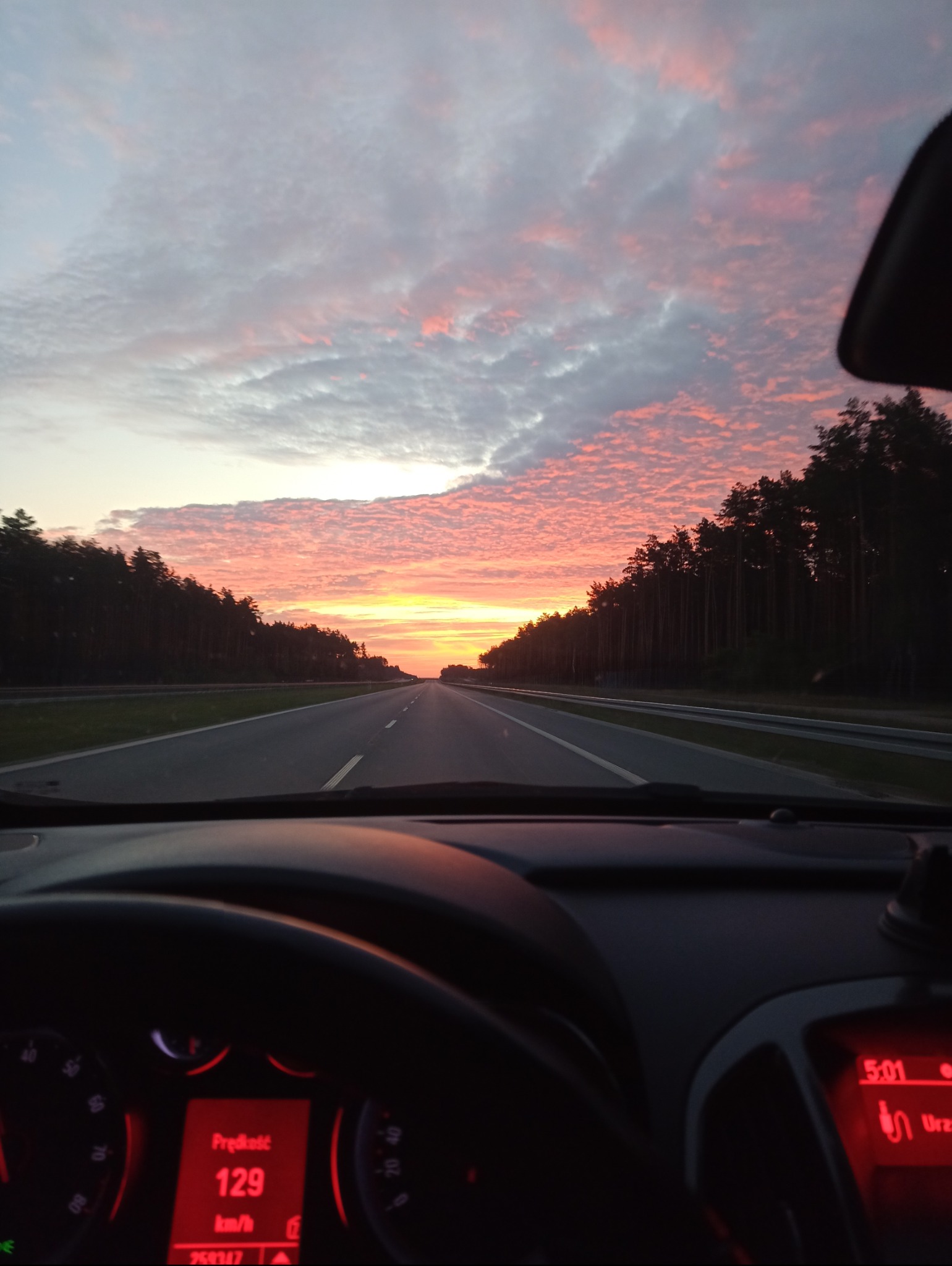 Widok z wnętrza samochodu na autostradę o wschodzie słońca, prędkość 129 km/h.