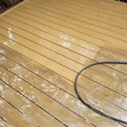 Drewniany taras częściowo pokryty pianą z węża podczas czyszczenia, ukazujący różnicę między czystą a brudną powierzchnią drewna.