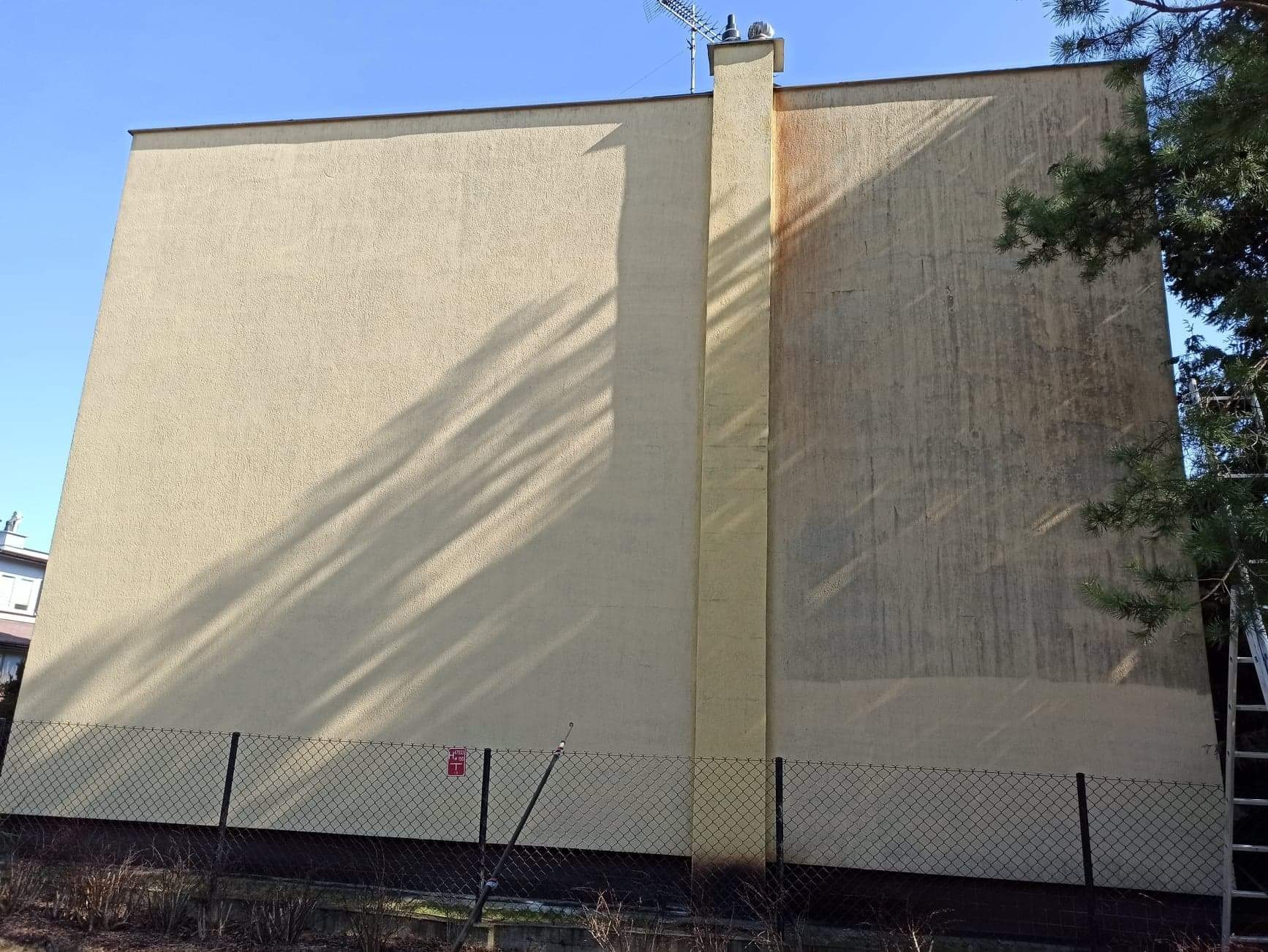 Fragment budynku z elewacją częściowo wyczyszczoną, widoczne różnice w kolorze i stopniu zabrudzenia, obok metalowa drabina oparta o ścianę.