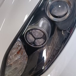 AUTO-DETAILING KAMIL KNOP - Błyszczący, biały lakier samochodu z reflektorem o futurystycznym designie, z widoczną strukturą wewnętrzną i odbiciami światła.