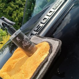 AUTO-DETAILING KAMIL KNOP - Błyszczący czarny lakier samochodu z emblematem 'HEMI 5.7L', na którym leży żółto-szara ściereczka z mikrofibry oraz butelka z rozpylaczem środka do pielęgnacji lakieru z motywem smoka.