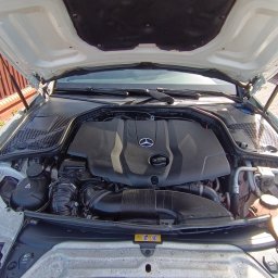 AUTO-DETAILING KAMIL KNOP - Otwarta maska białego samochodu marki Mercedes, ukazująca czysty i zadbany silnik. Widoczne elementy komory silnikowej i logo producenta.