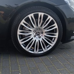 AUTO-DETAILING KAMIL KNOP - Błyszcząca felga aluminiowa z logo Mercedes-Benz na czarnej oponie, widoczna część karoserii auta na tle szarej kostki brukowej.