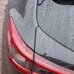 AUTO-DETAILING KAMIL KNOP - Czarny samochód, tylne światło i karoseria pokryte kroplami wody. Widoczny fragment tabliczki z nazwą modelu: Qashqai.
