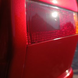 AUTO-DETAILING KAMIL KNOP - Błyszczący, czerwony lakier karoserii auta z widocznym tylnym światłem. Intensywne odbicie światła podkreśla głębię koloru i gładkość powierzchni.