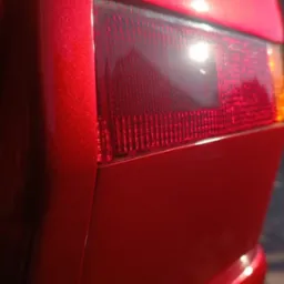 Błyszczący, czerwony lakier karoserii auta z widocznym tylnym światłem. Intensywne odbicie światła podkreśla głębię koloru i gładkość powierzchni.