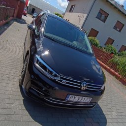 AUTO-DETAILING KAMIL KNOP - Błyszczący, czarny Volkswagen Touran R-Line, zaparkowany na brukowanej drodze, z widocznym numerem rejestracyjnym i odbiciem nieba w karoserii.