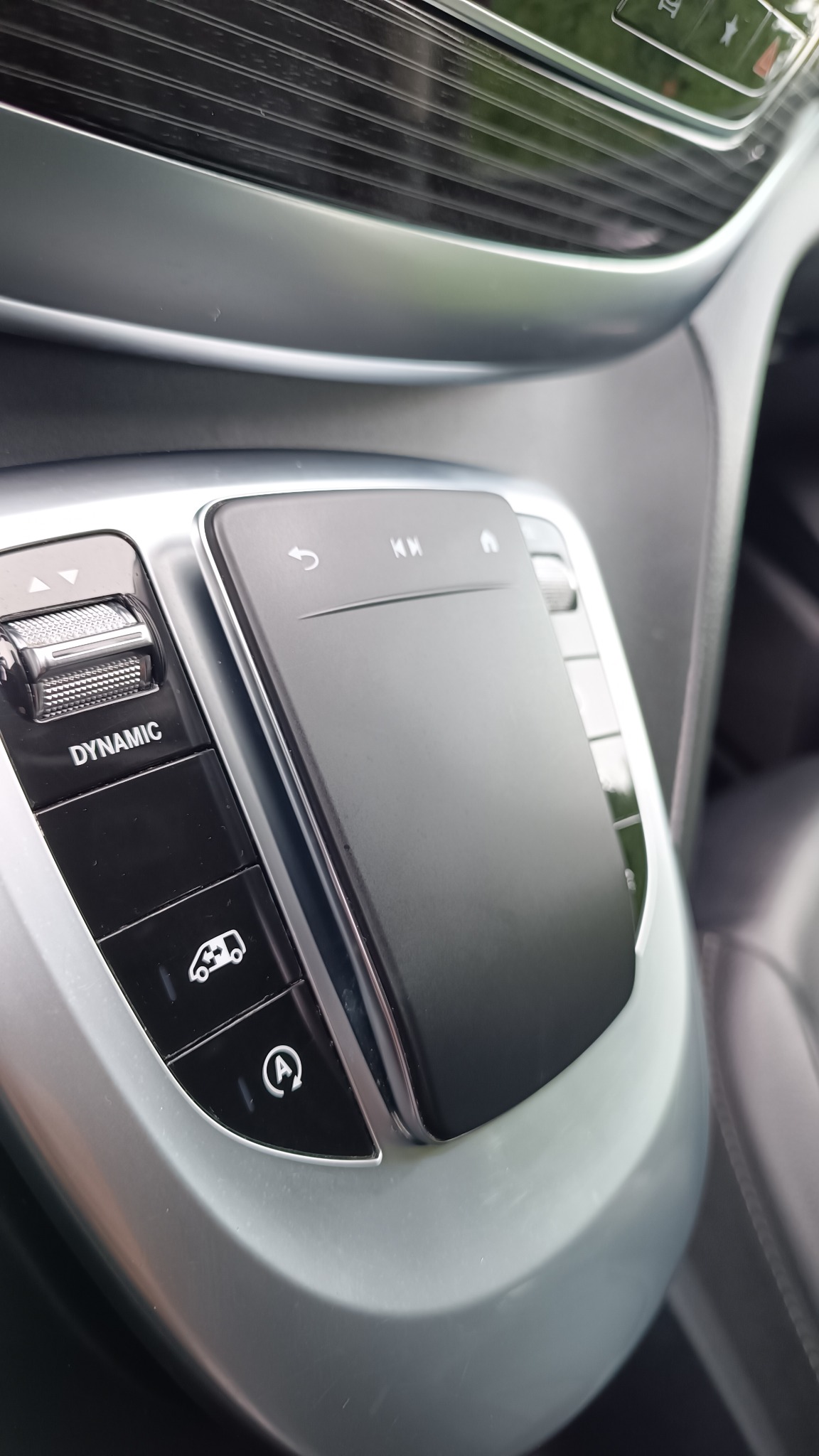 Panel sterowania w srebrnej obudowie pojazdu z przyciskami: Dynamic, auto start stop, oraz touchpad do sterowania multimediami.