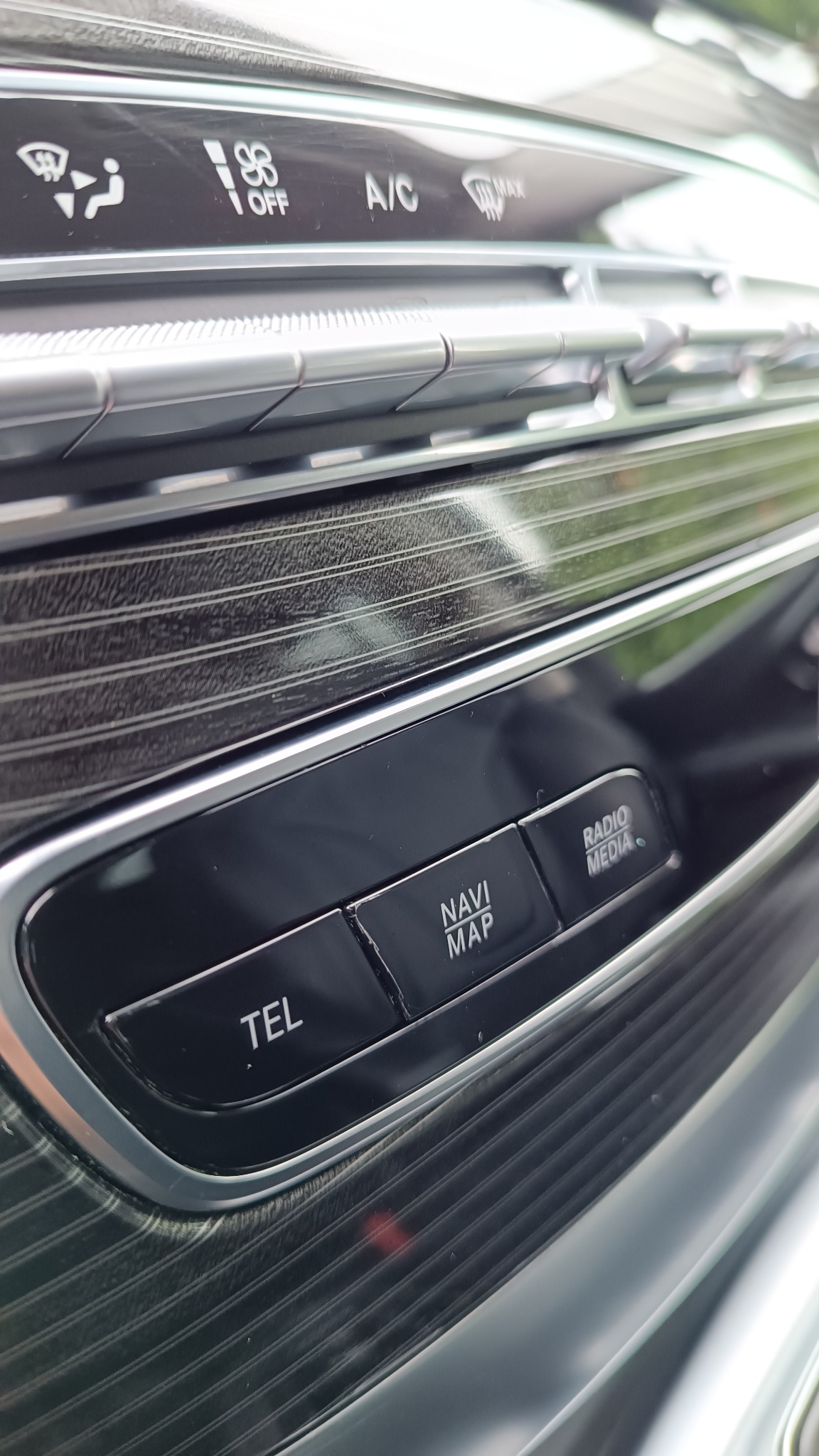 Detale wnętrza samochodu: panel sterowania z przyciskami nawigacji, telefonu i radia, srebrne wykończenia i tekstura imitująca drewno.