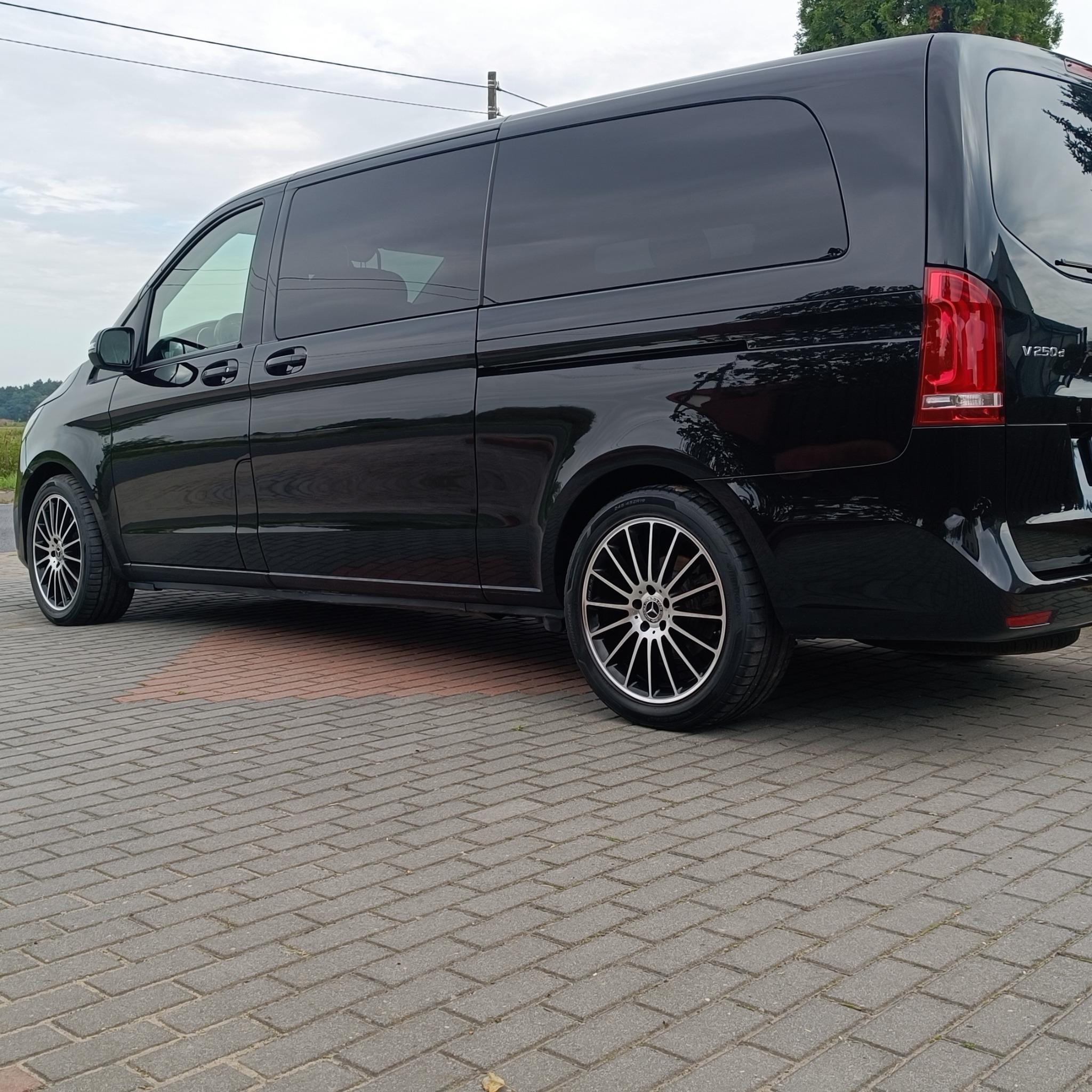 Błyszczący, czarny van Mercedes V250d po detailingu, zaparkowany na kostce brukowej. Widoczne felgi aluminiowe i odbicia w lakierze.
