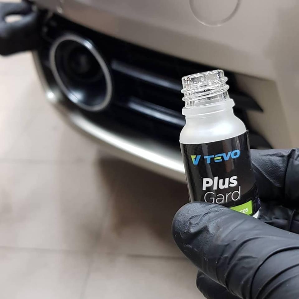 Aplikacja powłoki ochronnej TEVO Plus Gard na samochodzie w Wijewie. Buteleczka produktu w dłoni w czarnej rękawicy, widoczny fragment auta.