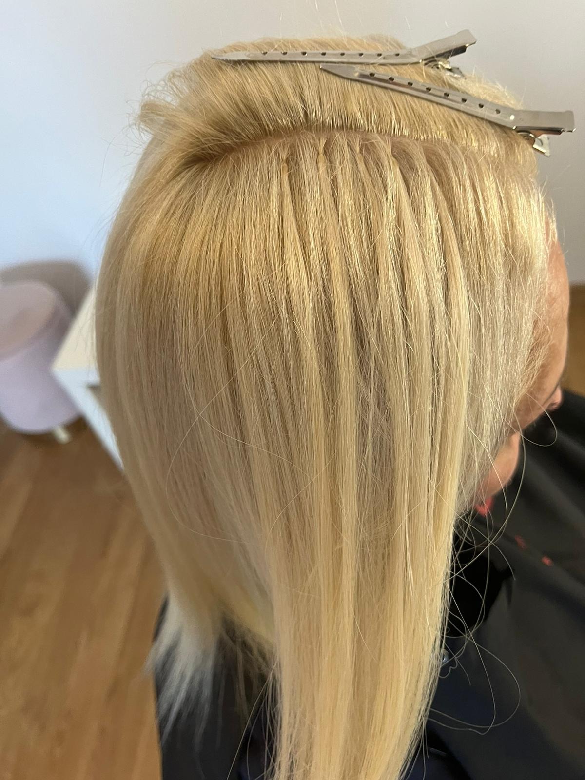 Blond włosy z wpiętymi metalowymi klipsami sekcyjnymi, przygotowane do zabiegu przedłużania lub zagęszczania włosów.