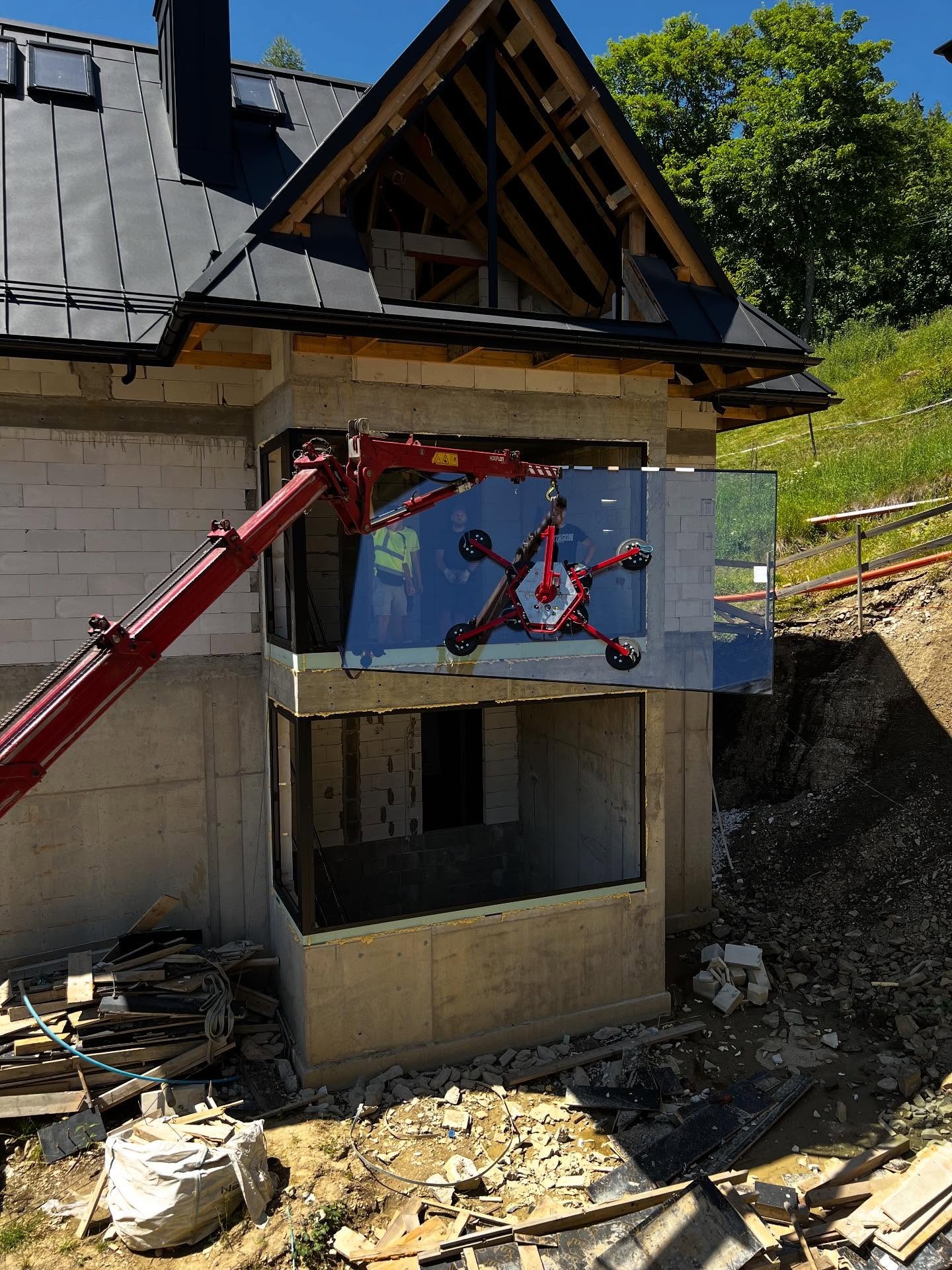 Montaż okna w surowym budynku z użyciem dźwigu ssącego. Widoczni pracownicy w odbiciu szyby. Budowa apartamentów w Zakopanem w tle.