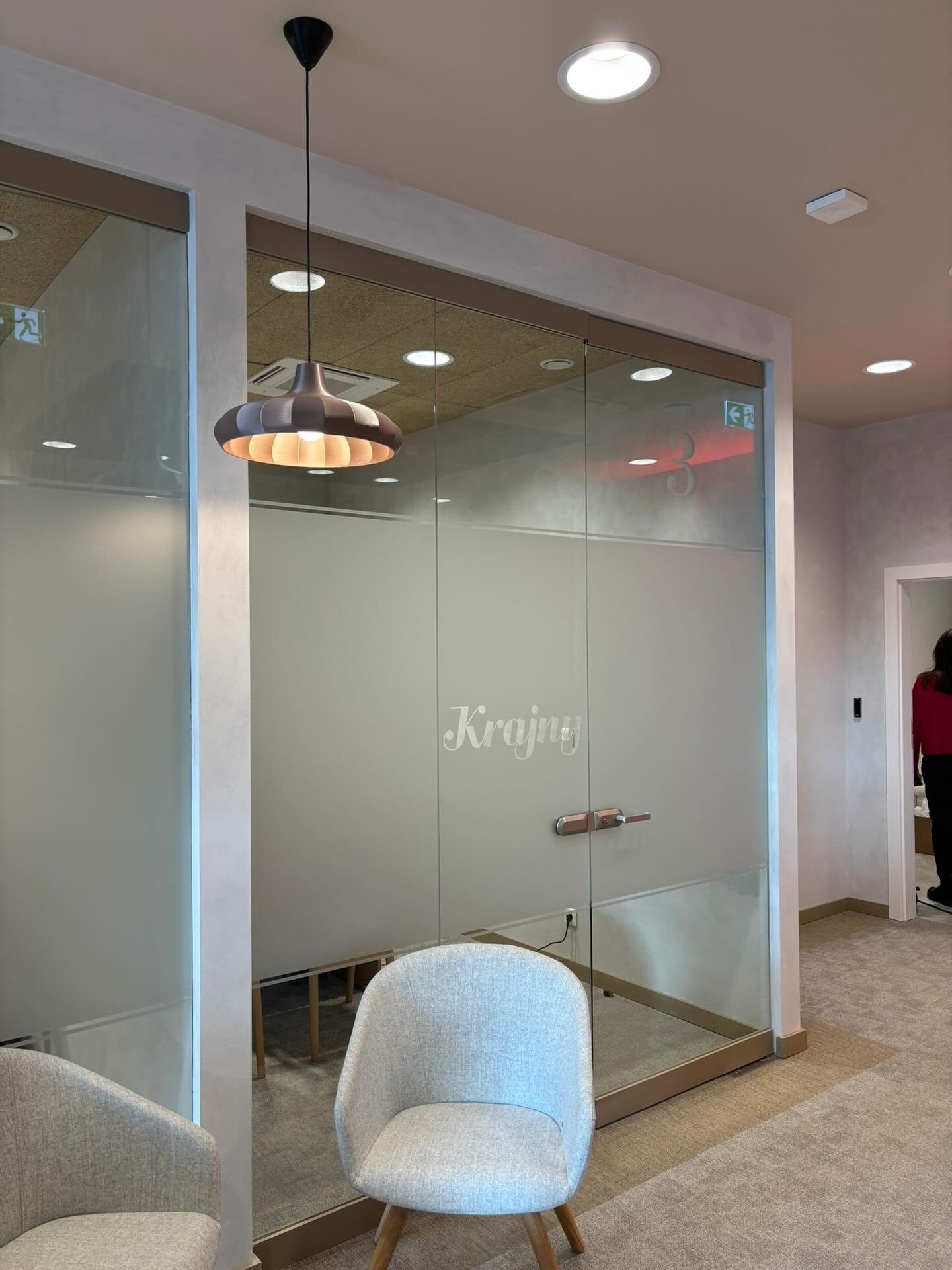 Szklana ścianka działowa z napisem 'Krajny' w biurze PEKOSA, oświetlona wiszącą lampą. Widoczne krzesła i fragment korytarza.