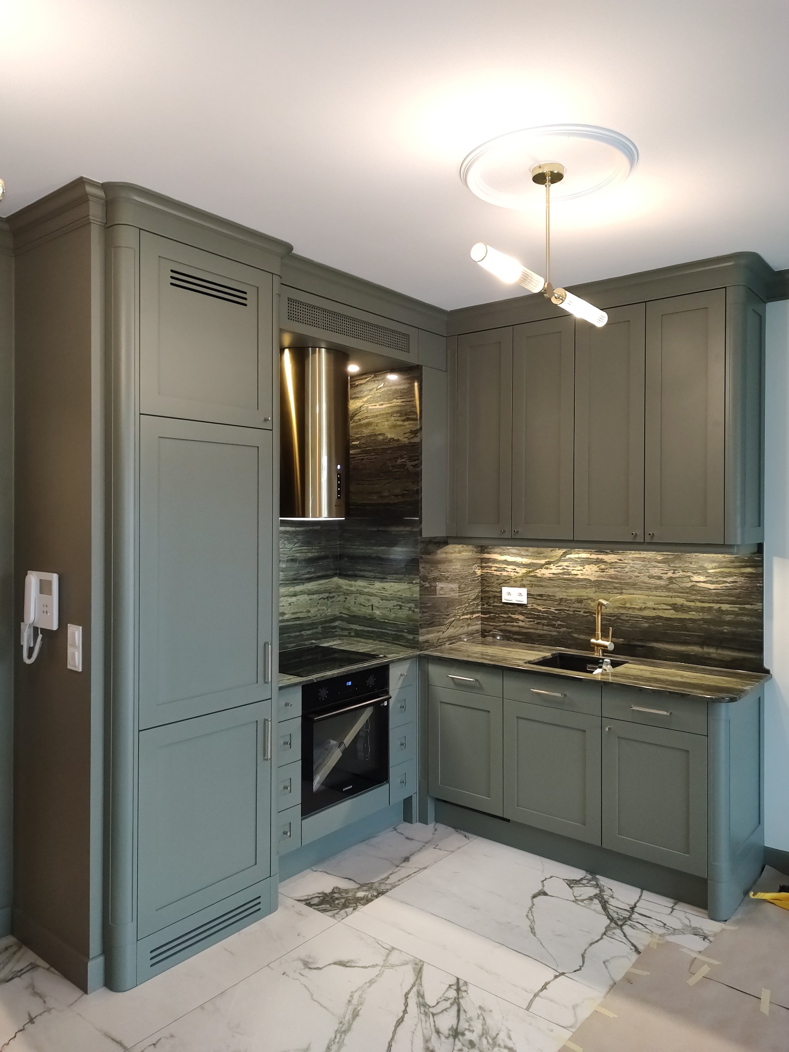 Nowoczesna kuchnia w odcieniach szarości z marmurowym blatem i podświetleniem, widoczny fragment podłogi z białego marmuru z ciemnymi żyłami i nowoczesna lampa sufitowa.