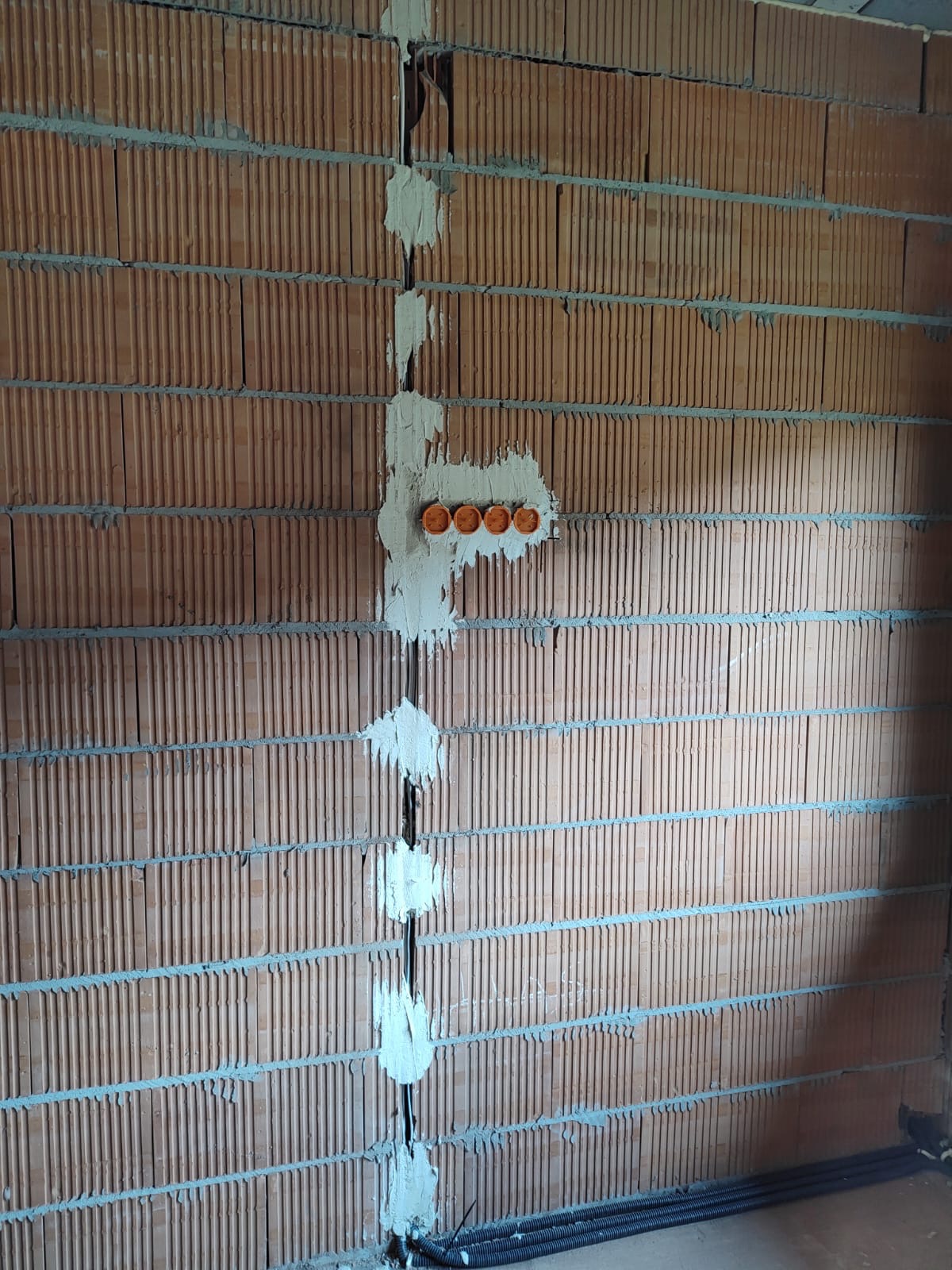 Ściana z cegły z wyżłobionymi kanałami elektrycznymi, w których umieszczono kable i puszki instalacyjne, zamurowane gipsem.