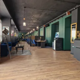 Nowoczesne biuro z ceglanym filarem, drewnianą podłogą, zielonymi ścianami i designerskim oświetleniem; widoczny fragment niebieskiej sofy i stolika kawowego.