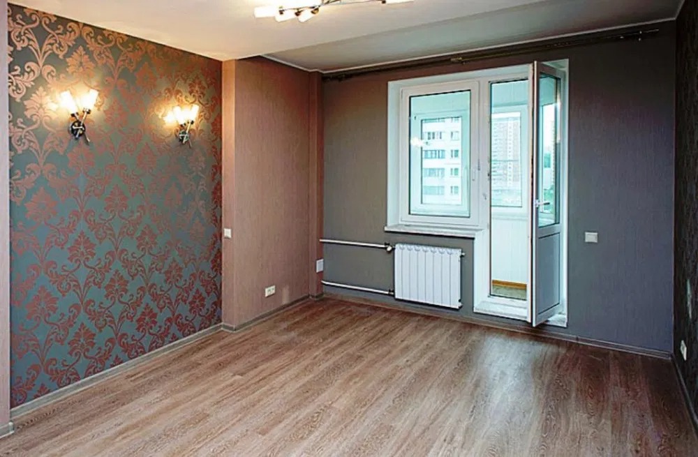 Pusty pokój po remoncie z nową podłogą z paneli, ozdobną tapetą w stylu vintage i balkonem z białymi ramami okiennymi.