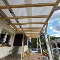 Pure NRG engineering - Montaż zadaszenia tarasu z drewnianą konstrukcją i folią izolacyjną, widoczny pracownik na drabinie, narzędzia oraz materiały budowlane na tarasie wyłożonym płytkami.