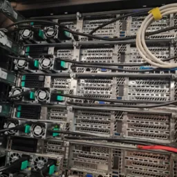 Widok z bliska na zainstalowane serwery w szafie rack, z widocznymi kablami zasilającymi i sieciowymi oraz wentylatorami chłodzącymi, ukazujący infrastrukturę IT.