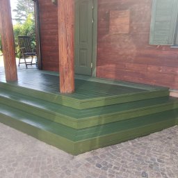 DRY HOUSE PAWEŁ SUSZYCKI - Zielone, drewniane schody wejściowe do domu z brązowymi ścianami i kolumnami. Widoczne okno z okiennicami i kamienna nawierzchnia.