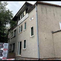 POL - DEK Sławomir Polesiak - Dwupiętrowy budynek z szarą elewacją przed rozpoczęciem prac. Widoczne paczki styropianu na pierwszym planie, przygotowane do ocieplenia.