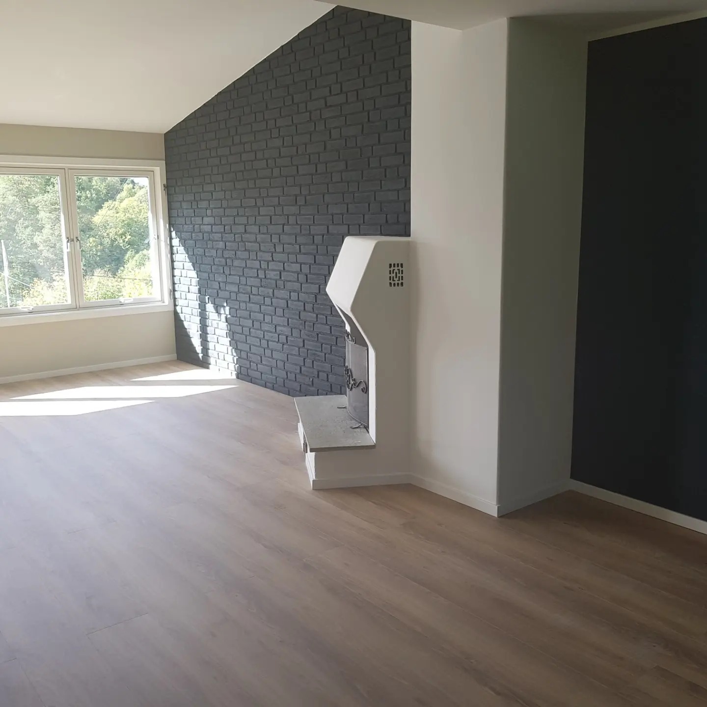 Wnętrze pokoju z jasną drewnianą podłogą, ścianą z ciemnej cegły, nowoczesnym białym kominkiem i ścianą pomalowaną na czarno, widok na zewnątrz przez okno.