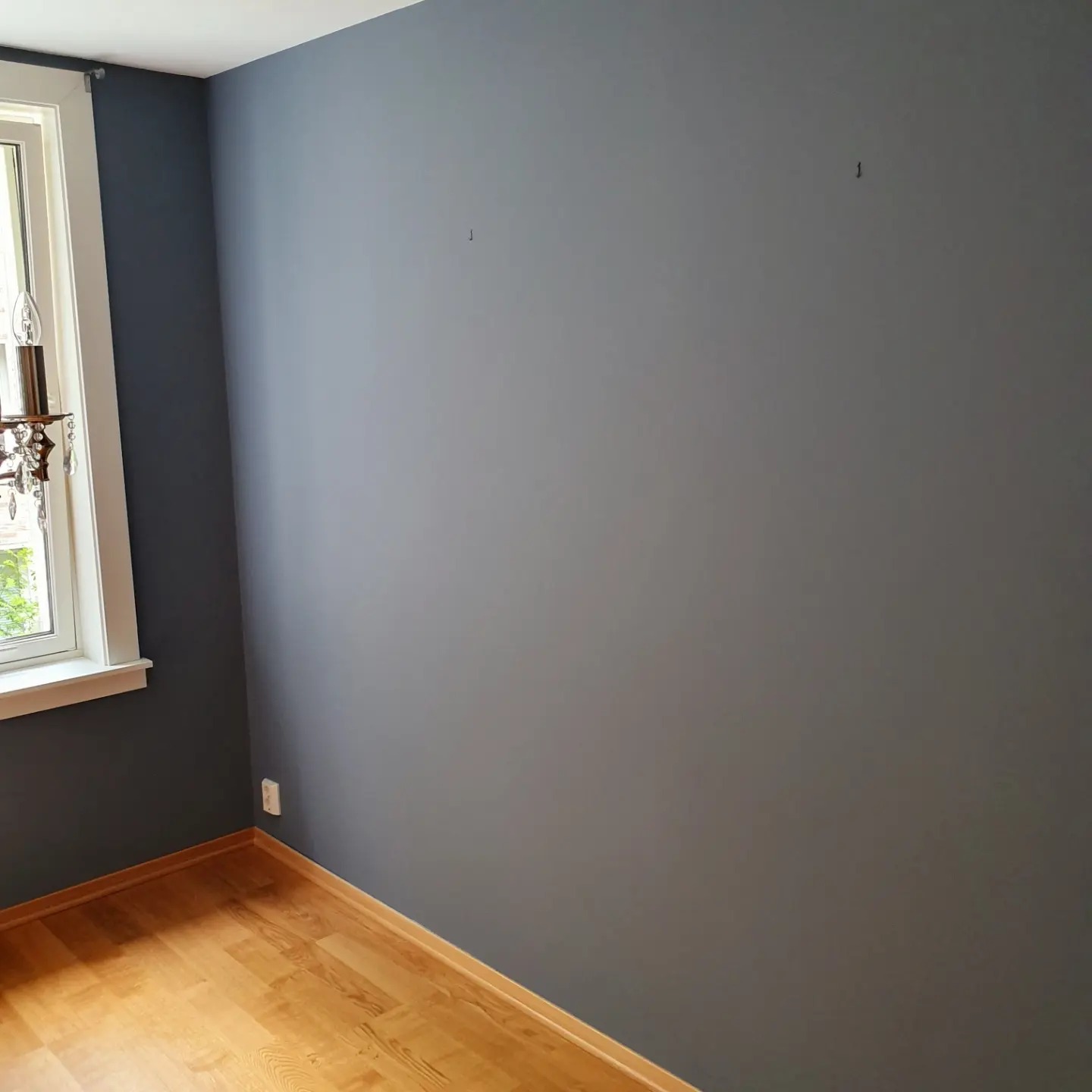 Świeżo pomalowany pokój w Rybniku z szarą ścianą i drewnianą podłogą, widoczny fragment okna z ozdobną lampą.