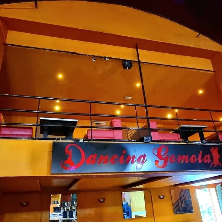 Wnętrze lokalu rozrywkowego z antresolą, pomalowane na pomarańczowo, z czarną balustradą i czerwonymi siedziskami. Widoczny szyld z nazwą 'Dancing Gomola' w czerwonej czcionce.