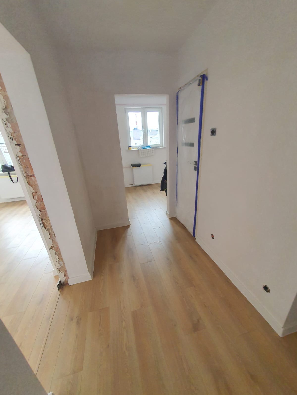 Ułożone panele podłogowe w mieszkaniu w Kole, drzwi zabezpieczone folią malarską, widoczne ślady po remoncie na ścianie.