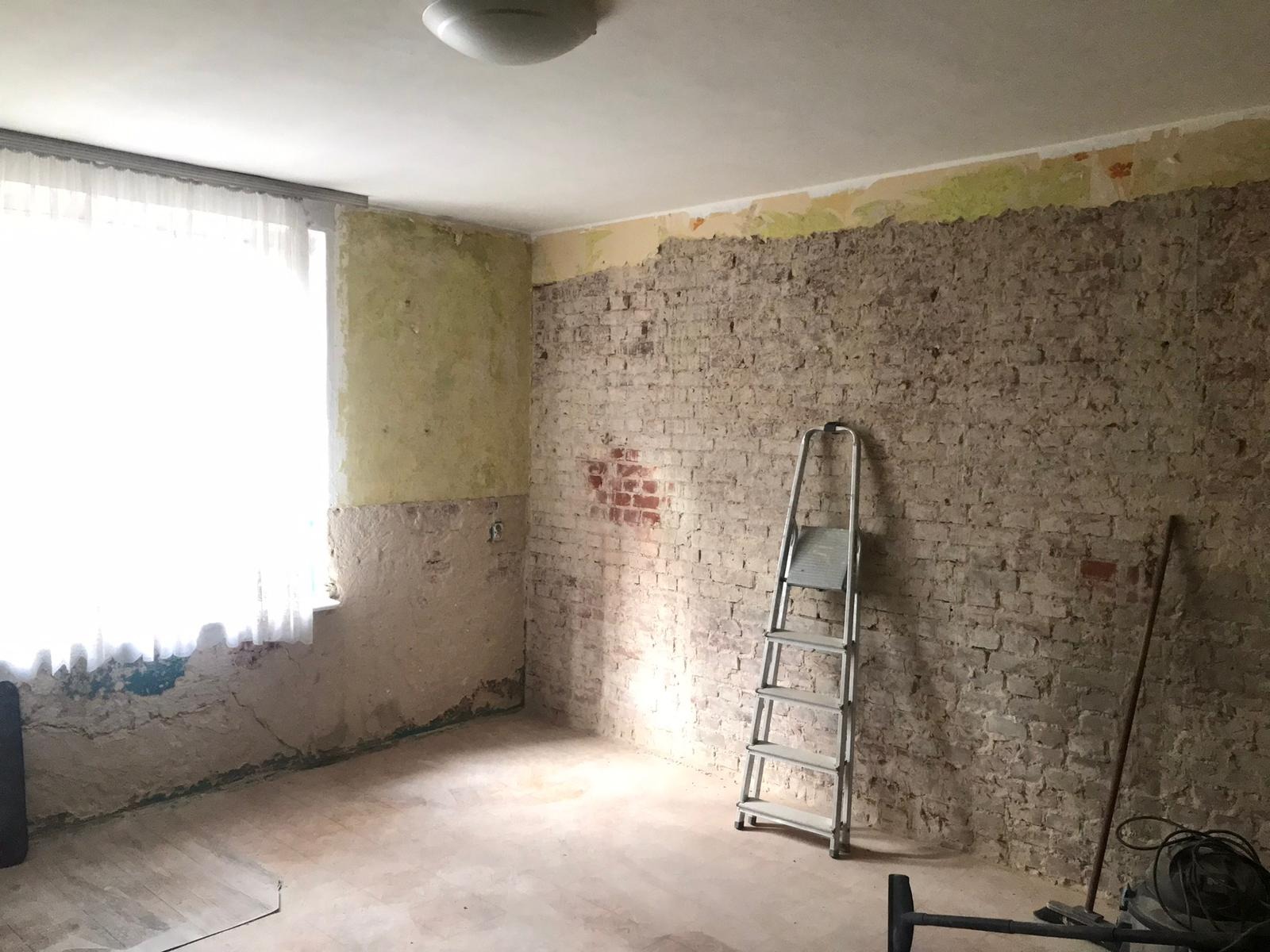 Pokój w trakcie remontu: odsłonięta cegła, częściowo usunięte stare powłoki, drabina oparta o ścianę, widoczne ślady wcześniejszych prac, przygotowanie do dalszych etapów wykończenia.