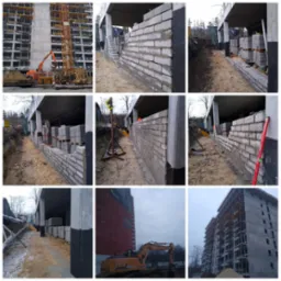 Wznoszenie ścian z bloczków betonowych na budowie wielopiętrowego budynku, widoczne palety z bloczkami, poziomica i narzędzia, w tle dźwig i maszyny budowlane.