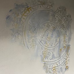 ELEWACJE I REMONTY ADAM CYRANIAK - Fragment ściany z dekoracyjnym, okrągłym wzorem malowanym szablonem w odcieniach szarości, błękitu i złota, częściowo zacierającym się na krawędziach.