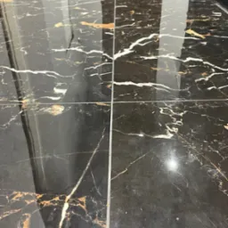 Błyszcząca posadzka z czarnych płytek imitujących marmur z wyraźnym, złotym i białym użyleniem, widoczne fugi i odbicie światła.