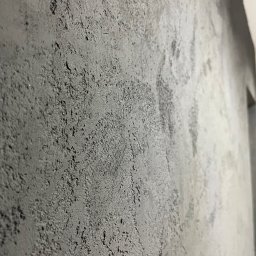 ELEWACJE I REMONTY ADAM CYRANIAK - Szara ściana z wyraźną, chropowatą fakturą, uchwycona pod kątem, z widocznymi nieregularnościami i subtelnymi refleksami światła.