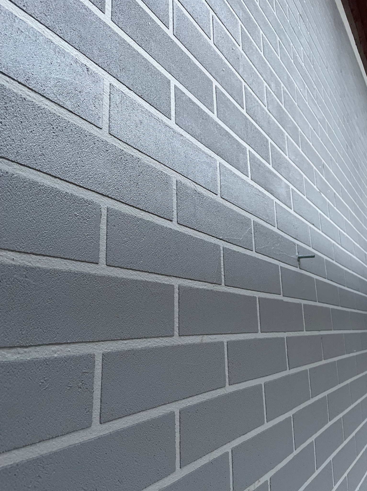 Szara ściana z cegieł pomalowana farbą elewacyjną, widoczny wystający gwóźdź.