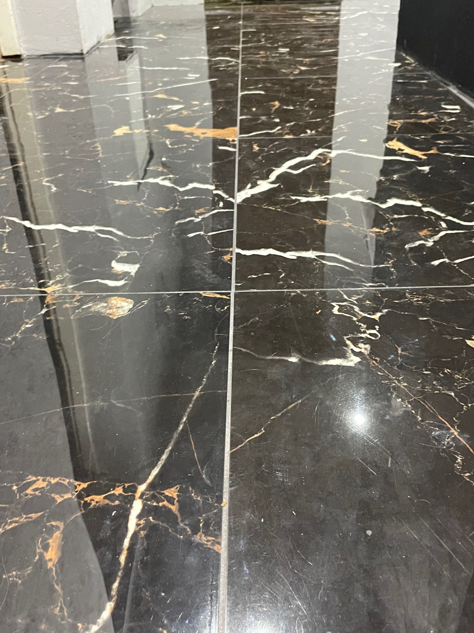 Błyszcząca posadzka z czarnych płytek imitujących marmur z wyraźnym, złotym i białym użyleniem, widoczne fugi i odbicie światła.