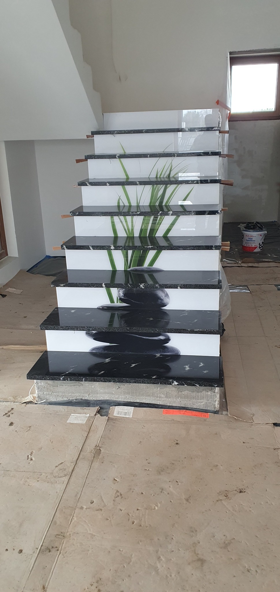 Nowoczesne schody z czarnymi kamiennymi stopniami z motywem zen, z widocznymi niedokończonymi pracami wykończeniowymi w tle.