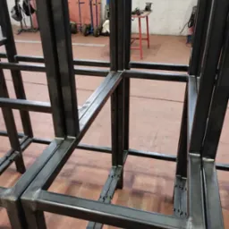 Surowa, spawana konstrukcja stalowa z profili zamkniętych, widoczne spawy, w tle wózek transportowy i narzędzia.